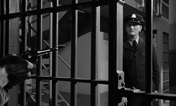 Movie still from “Birdman of Alcatraz” (1962), directed by John Frankenheimer – A man in a uniform standing behind a metal fence; Medium shot, Low angle