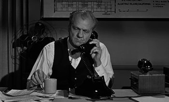 Movie still from “Birdman of Alcatraz” (1962), directed by John Frankenheimer – An older man sitting at a table talking on a phone; Medium shot, High angle