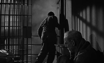Movie still from “Birdman of Alcatraz” (1962), directed by John Frankenheimer – A man standing next to a window next to another man; Medium shot, Low angle