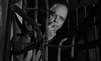 Movie still from “Birdman of Alcatraz” (1962), directed by John Frankenheimer – An old man with glasses is looking through bars of a jail cell; Medium shot, Low angle
