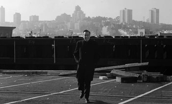 Movie still from “Birdman of Alcatraz” (1962), directed by John Frankenheimer – A man is walking in a parking lot in front of a city skyline; Medium shot, Low angle