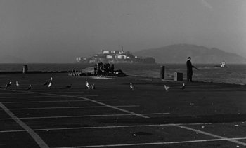 Movie still from “Birdman of Alcatraz” (1962), directed by John Frankenheimer – A black and white photo of a man standing in a parking lot; Extreme Wide shot, Low angle