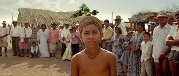 A young boy wearing a head dress in front of a group of people