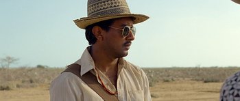 A man wearing a hat and sunglasses standing in the desert