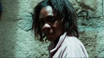 Movie still from “Biutiful” (2010), directed by Alejandro G. Iñárritu – A person with long hair is standing in front of a stone wall; Close Up shot, High angle