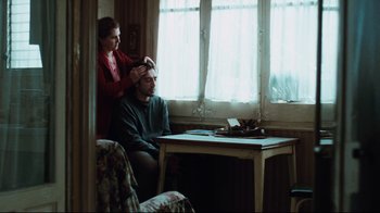 Movie still from “Biutiful” (2010), directed by Alejandro G. Iñárritu – A man sitting in front of a window while a woman puts his hair back; Medium shot, Over the shoulder angle
