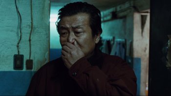 Movie still from “Biutiful” (2010), directed by Alejandro G. Iñárritu – A man in a red jacket is holding his hands to his face; Close Up shot, Low angle