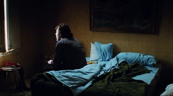 Movie still from “Biutiful” (2010), directed by Alejandro G. Iñárritu – A man sitting on a bed in a dark room; Medium shot, High angle