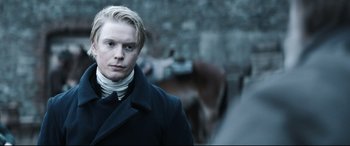 A man in a black coat standing in front of a horse