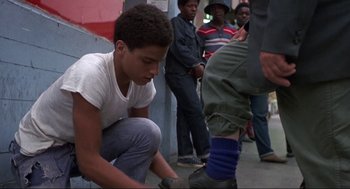 Movie still from “Black Caesar” (1973), directed by Larry Cohen – A young man kneeling down on the ground while a group of people watch; Medium shot, Low angle