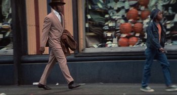 Movie still from “Black Caesar” (1973), directed by Larry Cohen – A man walking down the street wearing a suit and hat; Wide shot, Low angle