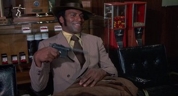 Movie still from “Black Caesar” (1973), directed by Larry Cohen – A man in a suit and hat holding a gun; Medium shot, Low angle