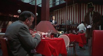 Movie still from “Black Caesar” (1973), directed by Larry Cohen – A man sitting at a table in a restaurant; Wide shot, Over the shoulder angle