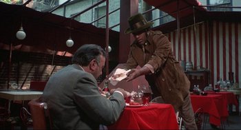 Movie still from “Black Caesar” (1973), directed by Larry Cohen – A man is serving a plate of food to another man; Medium shot, Over the shoulder angle