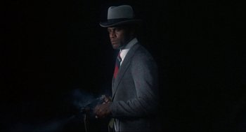 Movie still from “Black Caesar” (1973), directed by Larry Cohen – A man in a suit and hat holding a gun; Medium shot, Low angle
