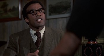 Movie still from “Black Caesar” (1973), directed by Larry Cohen – A man in a suit and tie talking to someone; Close Up shot, Over the shoulder angle