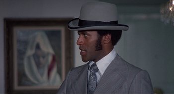 Movie still from “Black Caesar” (1973), directed by Larry Cohen – A man wearing a suit and a hat in front of a painting; Close Up shot, Low angle