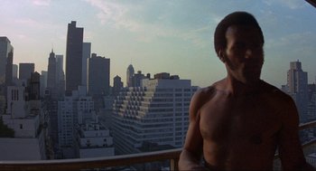 Movie still from “Black Caesar” (1973), directed by Larry Cohen – A man standing on top of a balcony next to buildings; Medium shot, Low angle