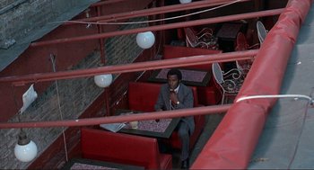 Movie still from “Black Caesar” (1973), directed by Larry Cohen – A man sitting on a red couch in a restaurant; Wide shot, High angle