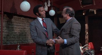 Movie still from “Black Caesar” (1973), directed by Larry Cohen – Two men in suits shaking hands in a restaurant; Medium shot, Low angle