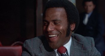 Movie still from “Black Caesar” (1973), directed by Larry Cohen – A man in a suit and tie smiling for the camera; Close Up shot, Low angle