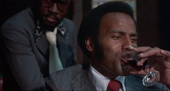 Movie still from “Black Caesar” (1973), directed by Larry Cohen – A man in a suit smoking a cigarette in front of another man in a suit; Close Up shot, Low angle