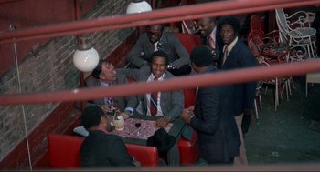 Movie still from “Black Caesar” (1973), directed by Larry Cohen – A group of men sitting around each other at a table; Wide shot, High angle