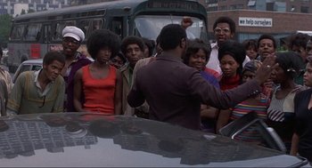 Movie still from “Black Caesar” (1973), directed by Larry Cohen – A group of people standing around a car; Medium shot, High angle