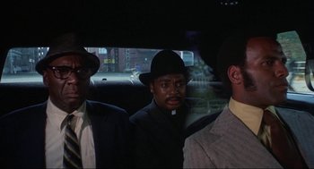 Movie still from “Black Caesar” (1973), directed by Larry Cohen – A group of men sitting in the back of a car; Close Up shot, Low angle