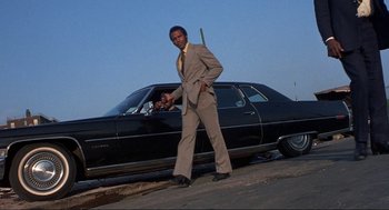 Movie still from “Black Caesar” (1973), directed by Larry Cohen – A man standing next to a car on the side of the road; Wide shot, Low angle