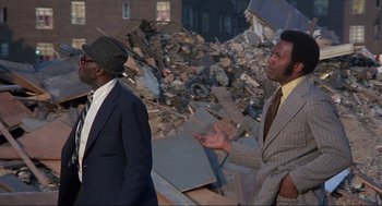 Movie still from “Black Caesar” (1973), directed by Larry Cohen – Two men in suits standing in front of a pile of rubble; Medium shot, Low angle