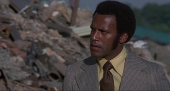 Movie still from “Black Caesar” (1973), directed by Larry Cohen – A man wearing a suit and tie standing in front of a pile of rubble; Close Up shot, Low angle