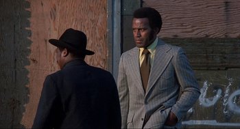 Movie still from “Black Caesar” (1973), directed by Larry Cohen – A man in a suit standing next to another man in a hat; Medium shot, Low angle
