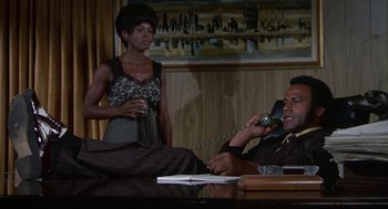Movie still from “Black Caesar” (1973), directed by Larry Cohen – A man and a woman sitting at a table talking on a phone; Medium shot, Low angle