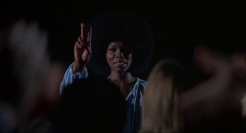Movie still from “Black Caesar” (1973), directed by Larry Cohen – A woman in a black hat is holding up a peace sign; Medium shot, Low angle