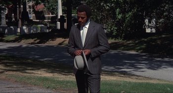Movie still from “Black Caesar” (1973), directed by Larry Cohen – A man in a suit and tie holding a hat; Medium shot, Low angle