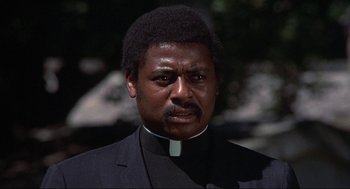 Movie still from “Black Caesar” (1973), directed by Larry Cohen – A person wearing a priest's outfit; Close Up shot, Low angle