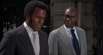 Movie still from “Black Caesar” (1973), directed by Larry Cohen – Two men in business suits standing next to each other; Close Up shot, Low angle