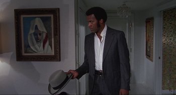 Movie still from “Black Caesar” (1973), directed by Larry Cohen – A man in a suit holding onto a white hat; Medium shot, Low angle