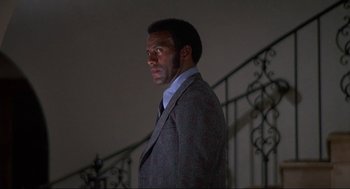 Movie still from “Black Caesar” (1973), directed by Larry Cohen – A man in a suit and tie standing in front of a railing; Medium shot, Low angle