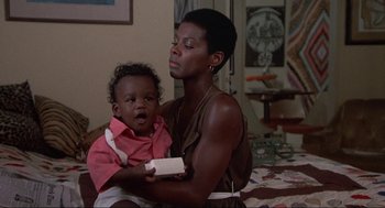 Movie still from “Black Caesar” (1973), directed by Larry Cohen – A woman holding a baby in her arms; Medium shot, Low angle