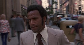 Movie still from “Black Caesar” (1973), directed by Larry Cohen – A man wearing a suit and tie on a city street; Close Up shot, Low angle
