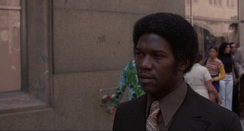 Movie still from “Black Caesar” (1973), directed by Larry Cohen – A man in a suit and tie standing in front of a wall; Close Up shot, Low angle