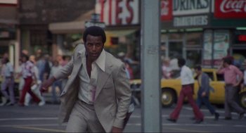 Movie still from “Black Caesar” (1973), directed by Larry Cohen – A man in a suit and tie walking down a street; Medium shot, Low angle
