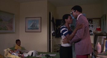 Movie still from “Black Caesar” (1973), directed by Larry Cohen – A man and a woman standing next to each other in a living room; Wide shot, Over the shoulder angle