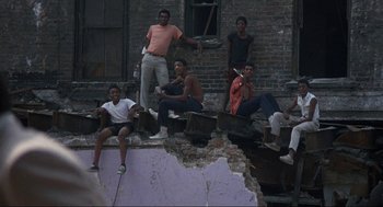 Movie still from “Black Caesar” (1973), directed by Larry Cohen – A group of young men sitting on the side of a building; Wide shot, High angle