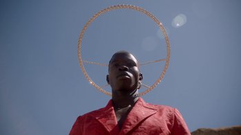 Movie still from “Black Is King” (2020), directed by Julian Klincewicz – A man in a red jacket with a large hoop around his head; Close Up shot, Low angle