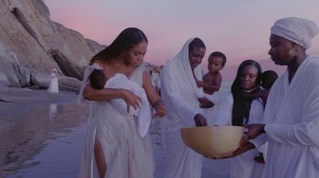 Movie still from “Black Is King” (2020), directed by Julian Klincewicz – A group of people standing on top of a sandy beach; Medium shot, Low angle