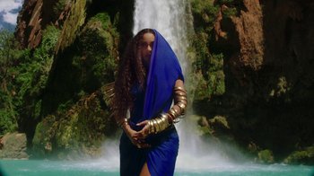 Movie still from “Black Is King” (2020), directed by Julian Klincewicz – A woman in a blue dress standing in front of a waterfall; Wide shot, Low angle