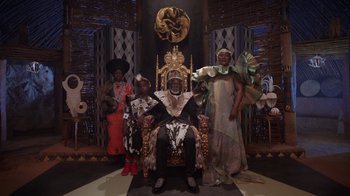 Movie still from “Black Is King” (2020), directed by Julian Klincewicz – A man sitting on top of a throne in front of a group of people; Wide shot, Low angle